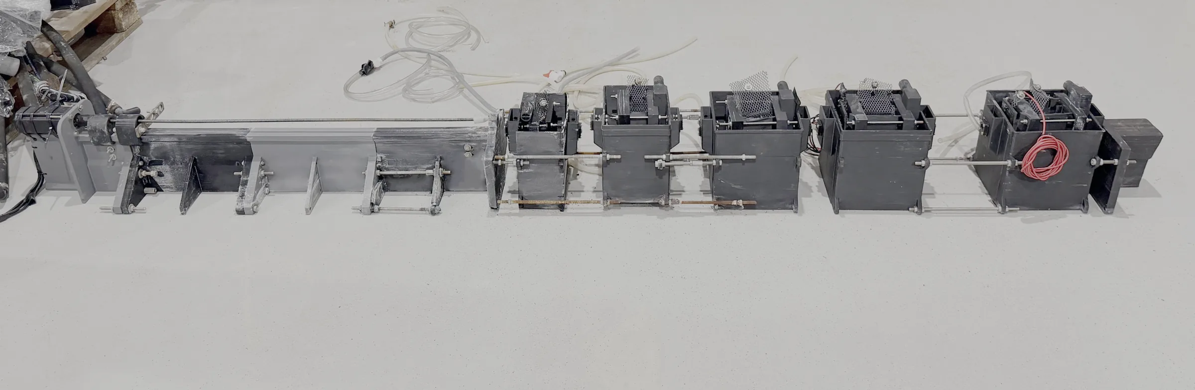 The self-built 3D-printed pilot line seen from the side: a row of black printed cells on a rail, on a concrete floor