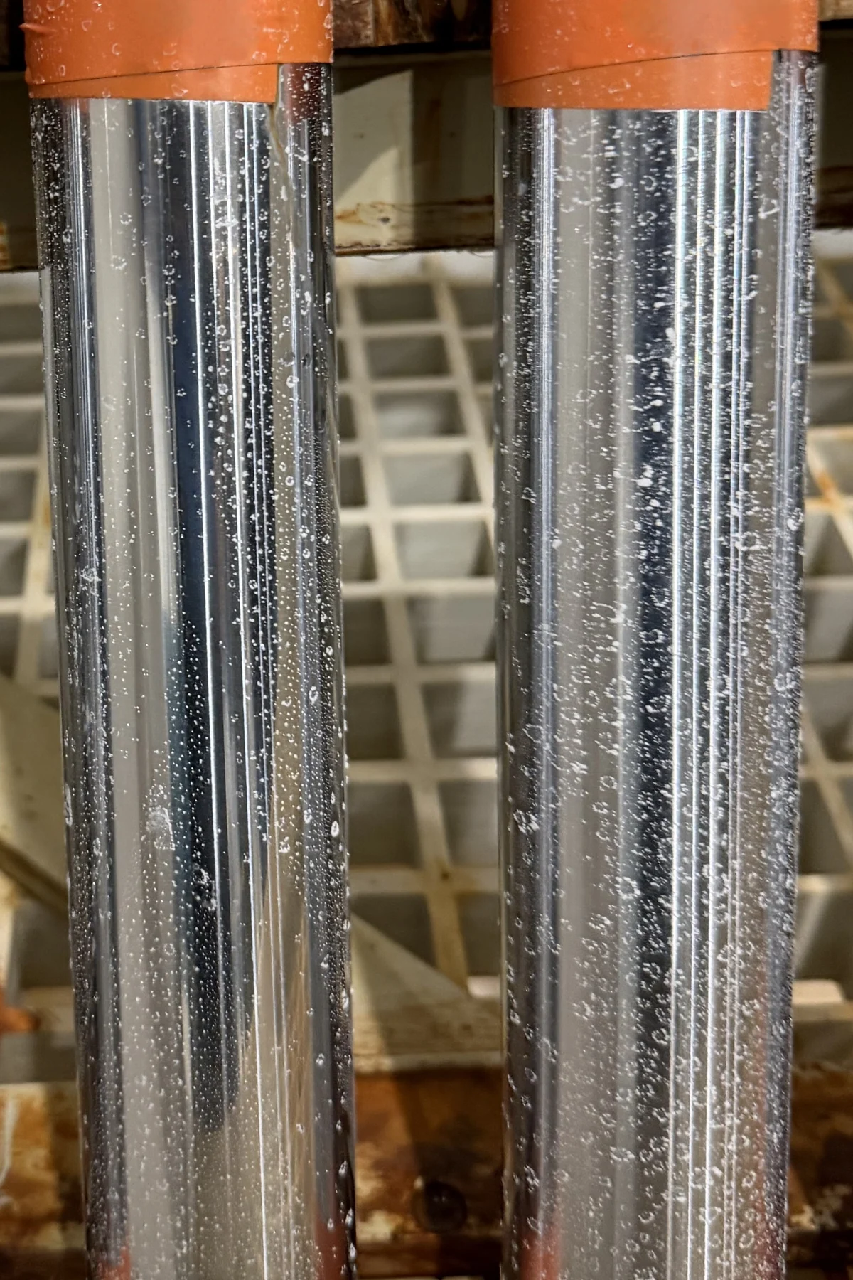 Two TripleHard® coated rods standing in a salt spray chamber after 250 hours, bright and beaded with droplets, no rust